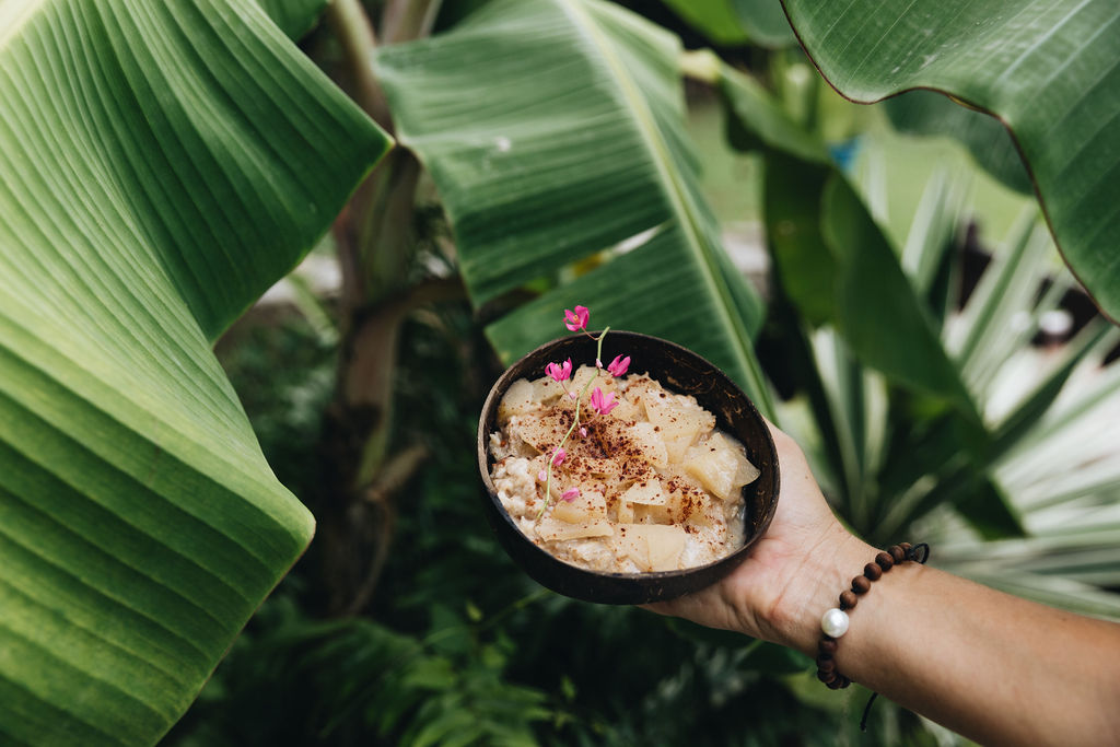 A hand holding a bowl of herbal preparation among green leaves